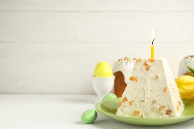 Photo of Traditional cottage cheese Easter paskha with dried apricot and burning candle on white wooden table, space for text