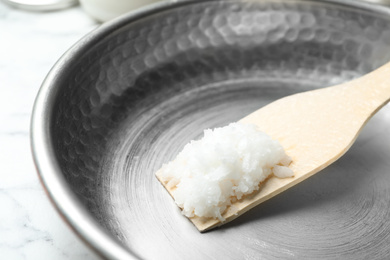 Frying pan with coconut oil and wooden spatula on white marble table, closeup. Healthy cooking