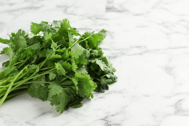 Photo of Bunch of fresh aromatic cilantro on white marble table. Space for text