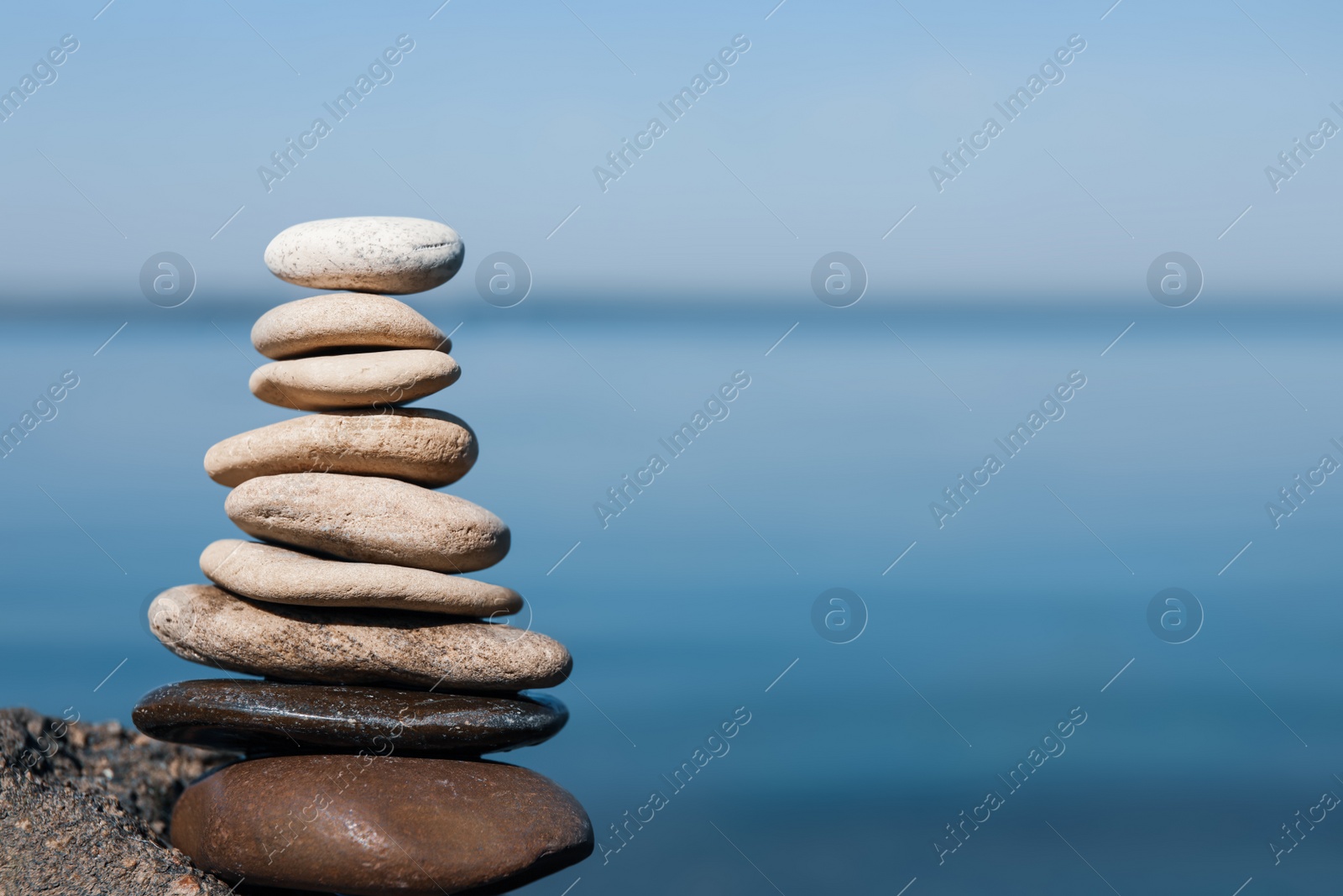 Photo of Stack of stones on rock near sea, space for text. Harmony and balance concept