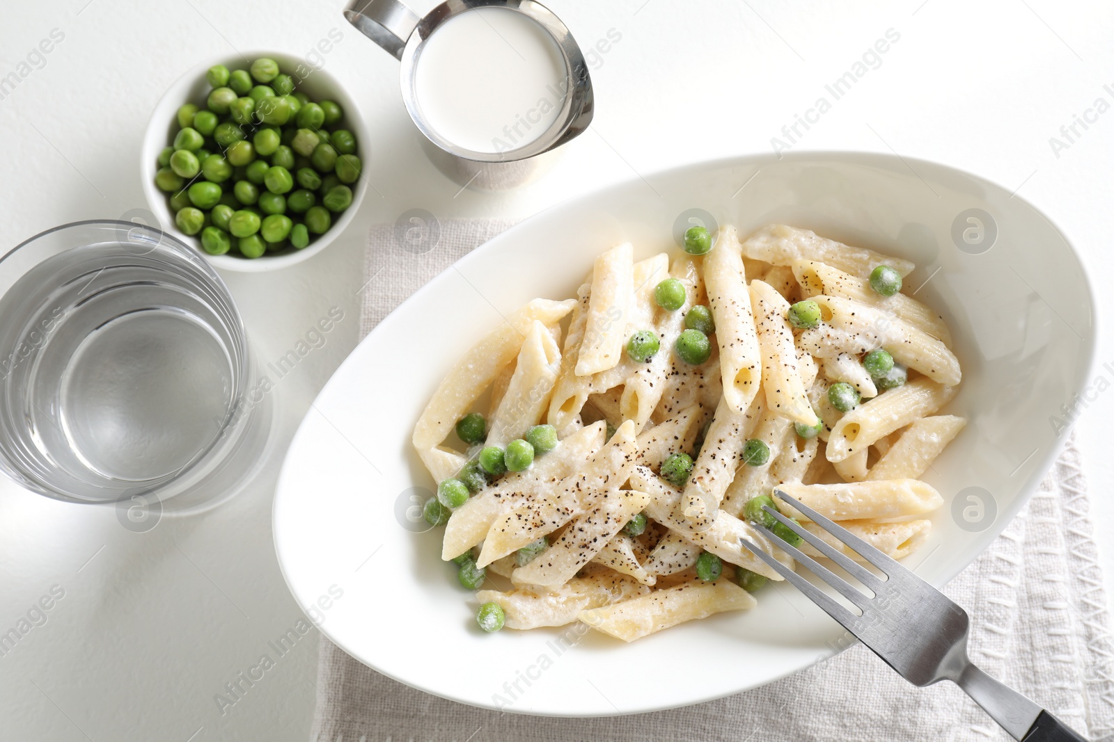 Photo of Delicious pasta with green peas, creamy sauce, water and fork on white table, top view