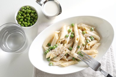 Photo of Delicious pasta with green peas, creamy sauce, water and fork on white table, top view