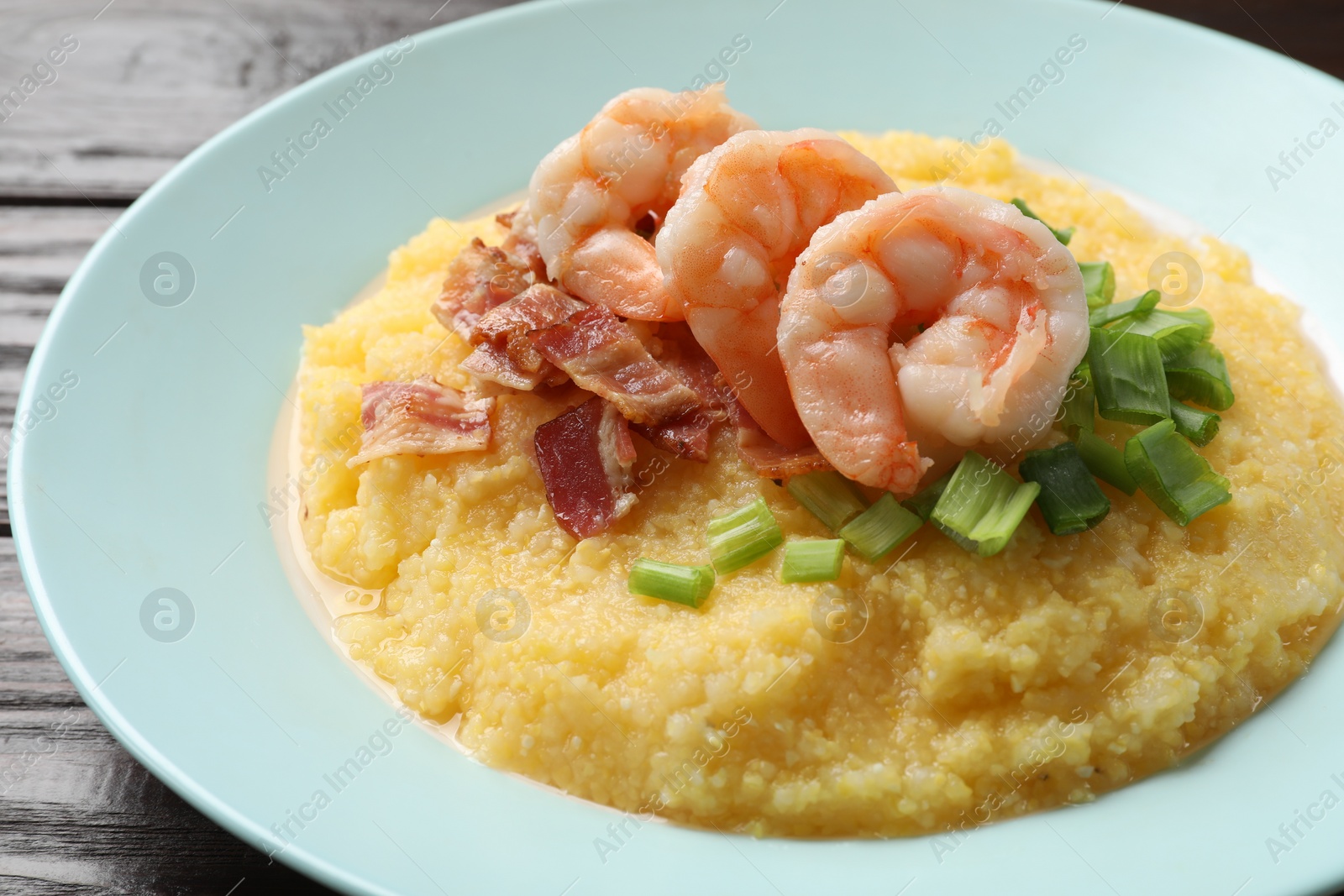 Photo of Plate with fresh tasty shrimps, bacon and grits on dark wooden table, closeup