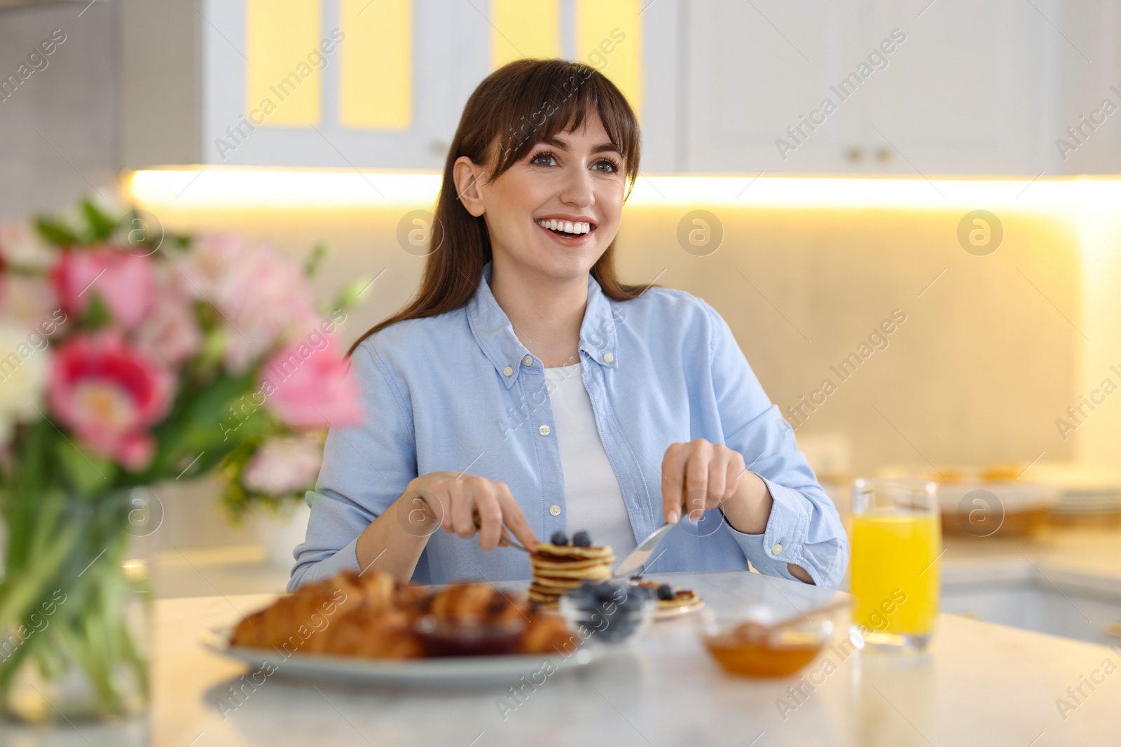 Photo of Smiling woman eating tasty pancakes at breakfast indoors
