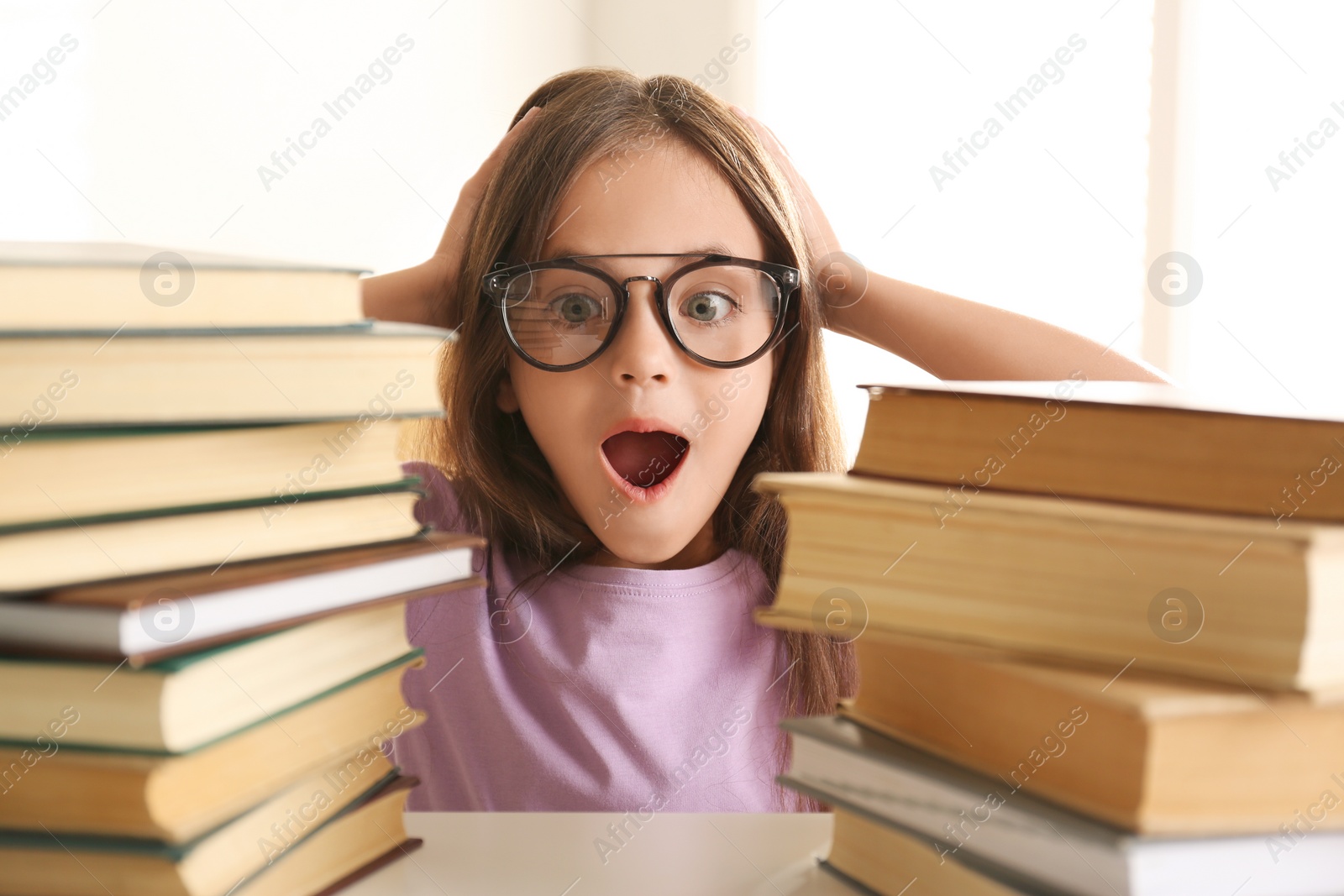 Photo of Emotional little girl at table with books. Doing homework