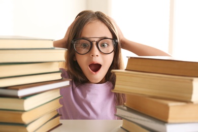 Photo of Emotional little girl at table with books. Doing homework