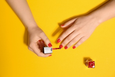 Woman applying nail polish on color background, top view