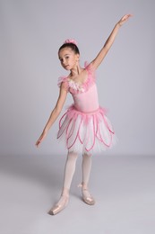 Photo of Beautifully dressed little ballerina dancing on grey background