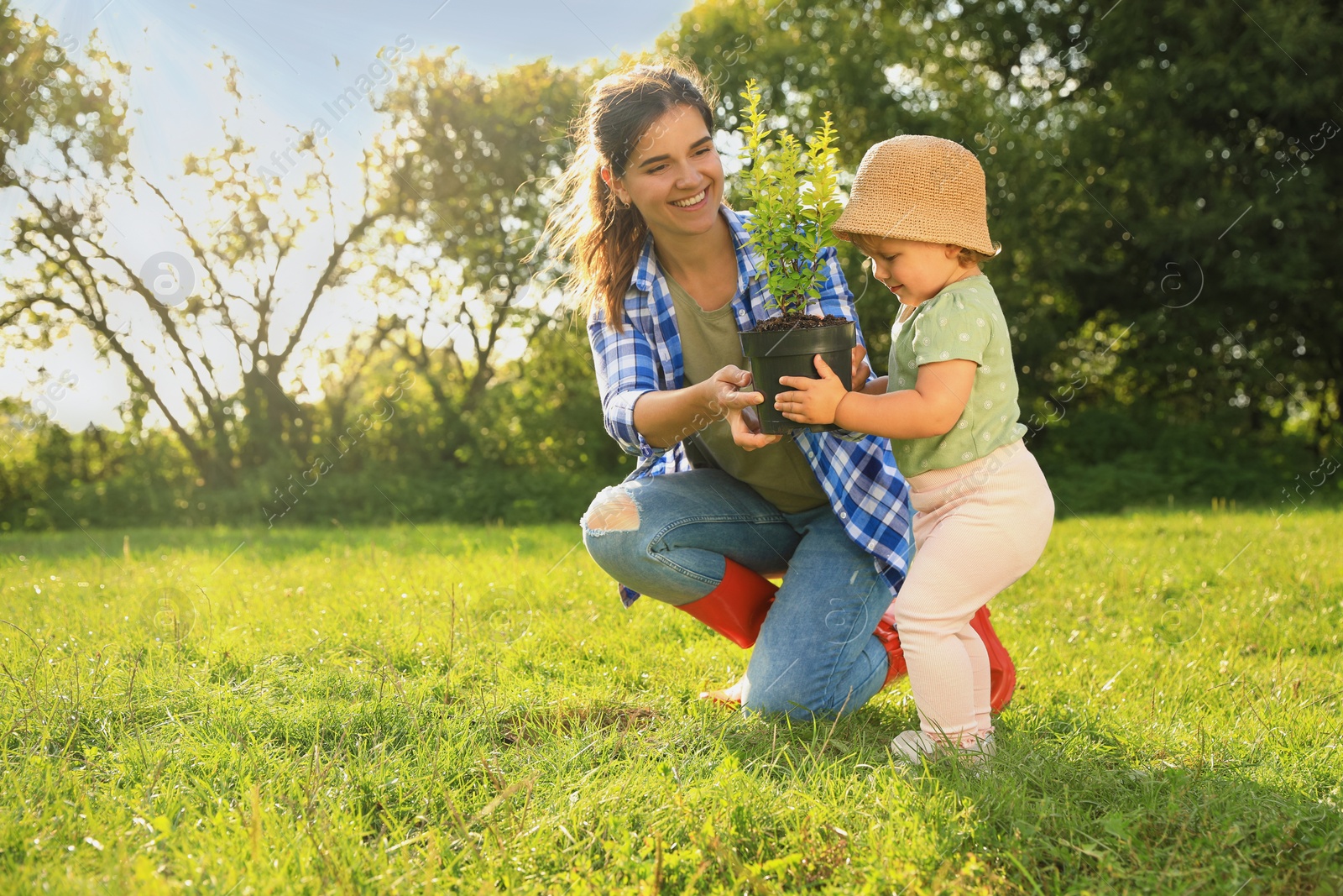 Photo of Mother and her baby daughter planting tree together in garden, space for text