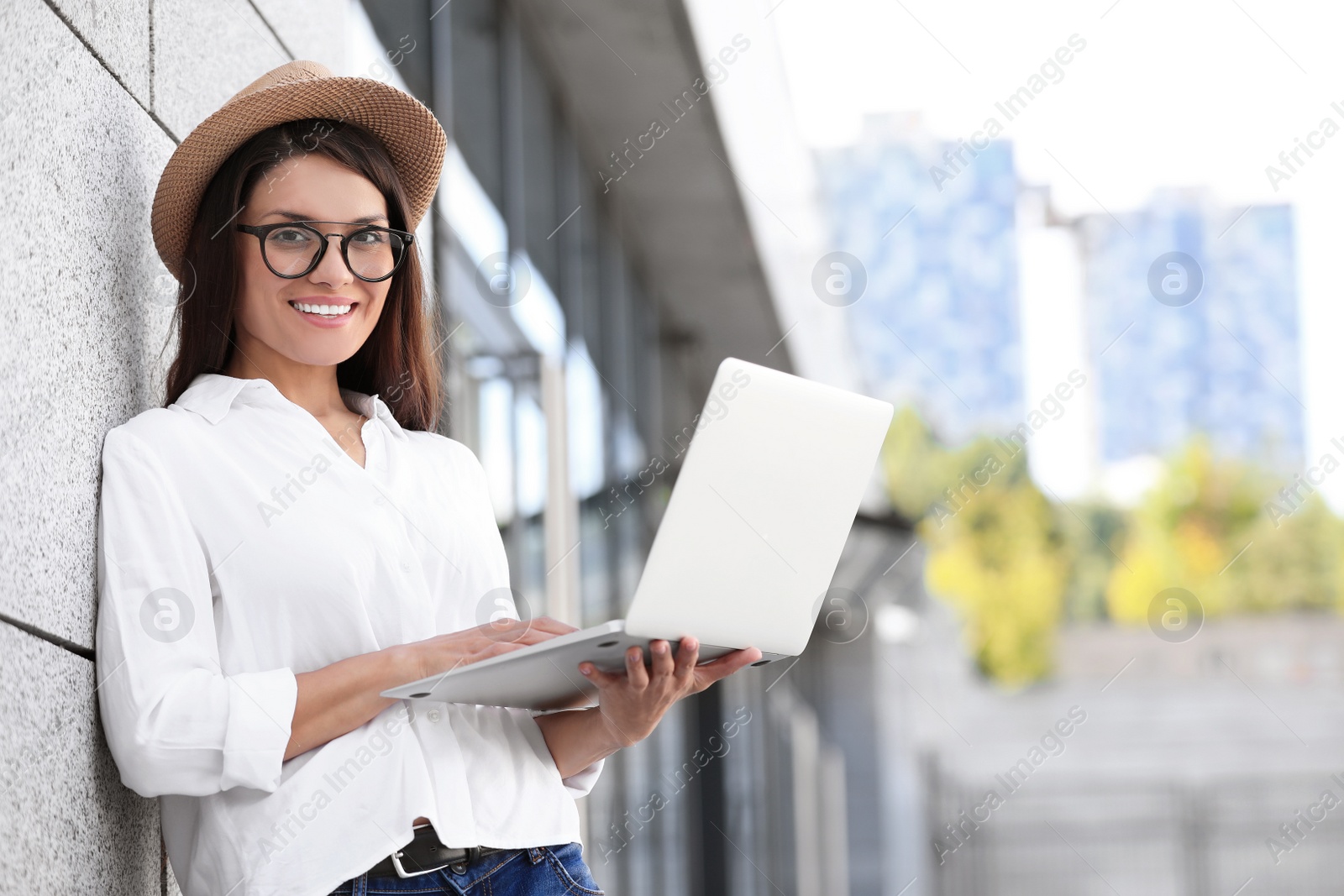 Photo of Beautiful woman using laptop on city street. Space for text
