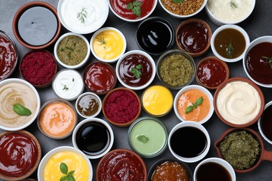 Many different sauces and herbs on black table, flat lay