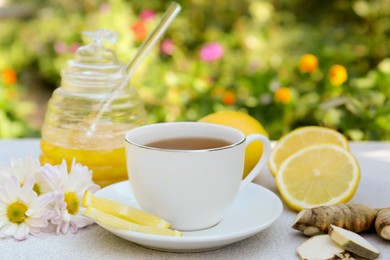 Cup of delicious tea with honey, lemon and ginger on white table outdoors