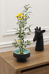 Stylish ikebana with beautiful yellow flowers, green branch and decor carrying cozy atmosphere at home