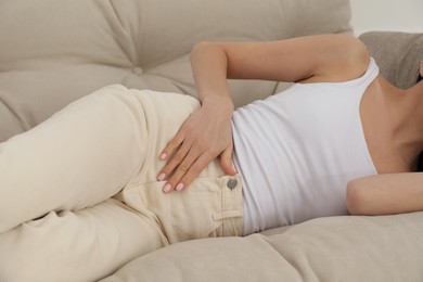 Photo of Woman suffering from appendicitis inflammation on sofa indoors, closeup