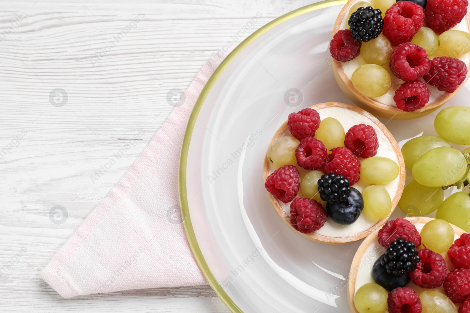 Photo of Delicious tartlets with berries on white wooden table, top view