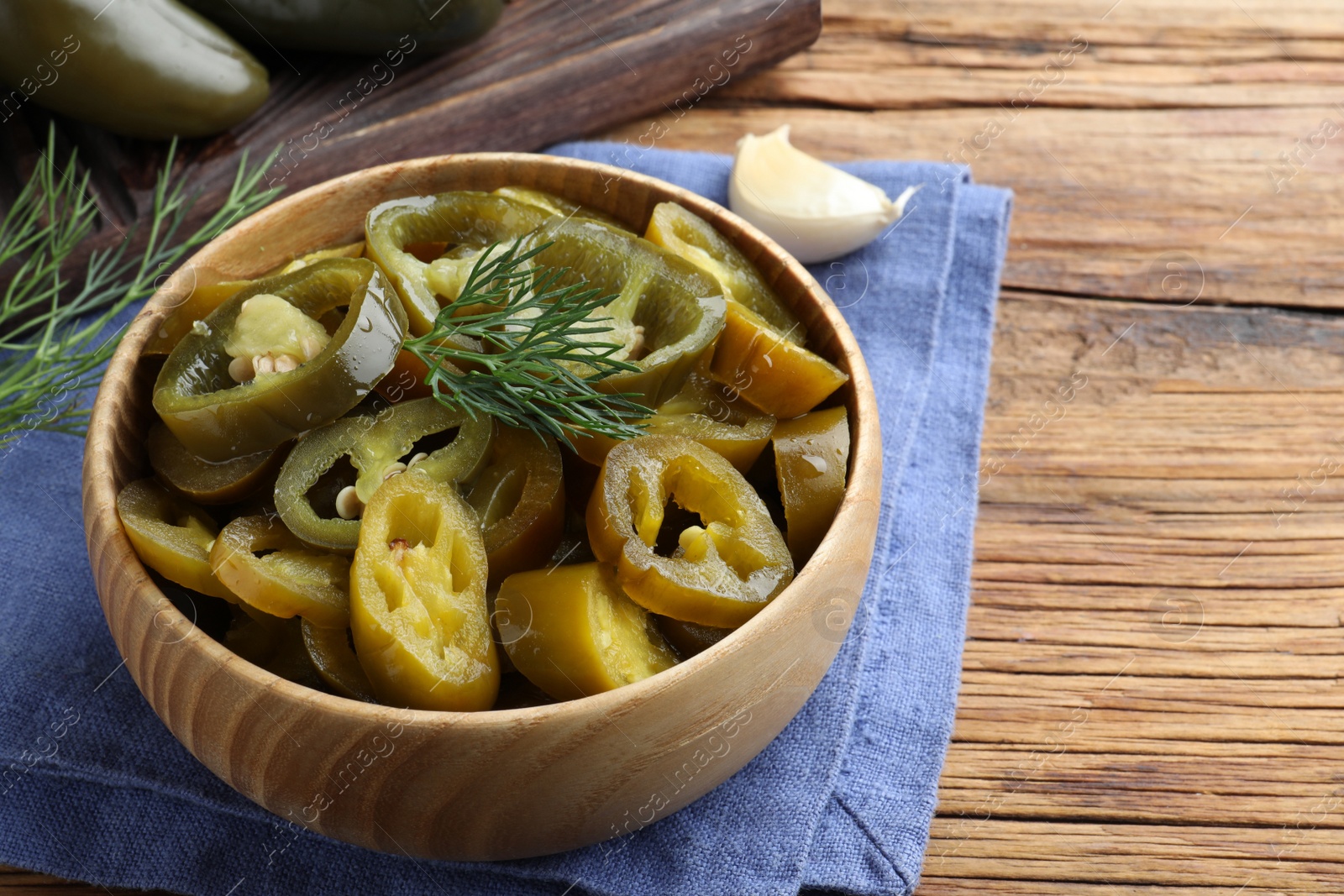 Photo of Bowl with slices of pickled green jalapeno peppers on wooden table, space for text