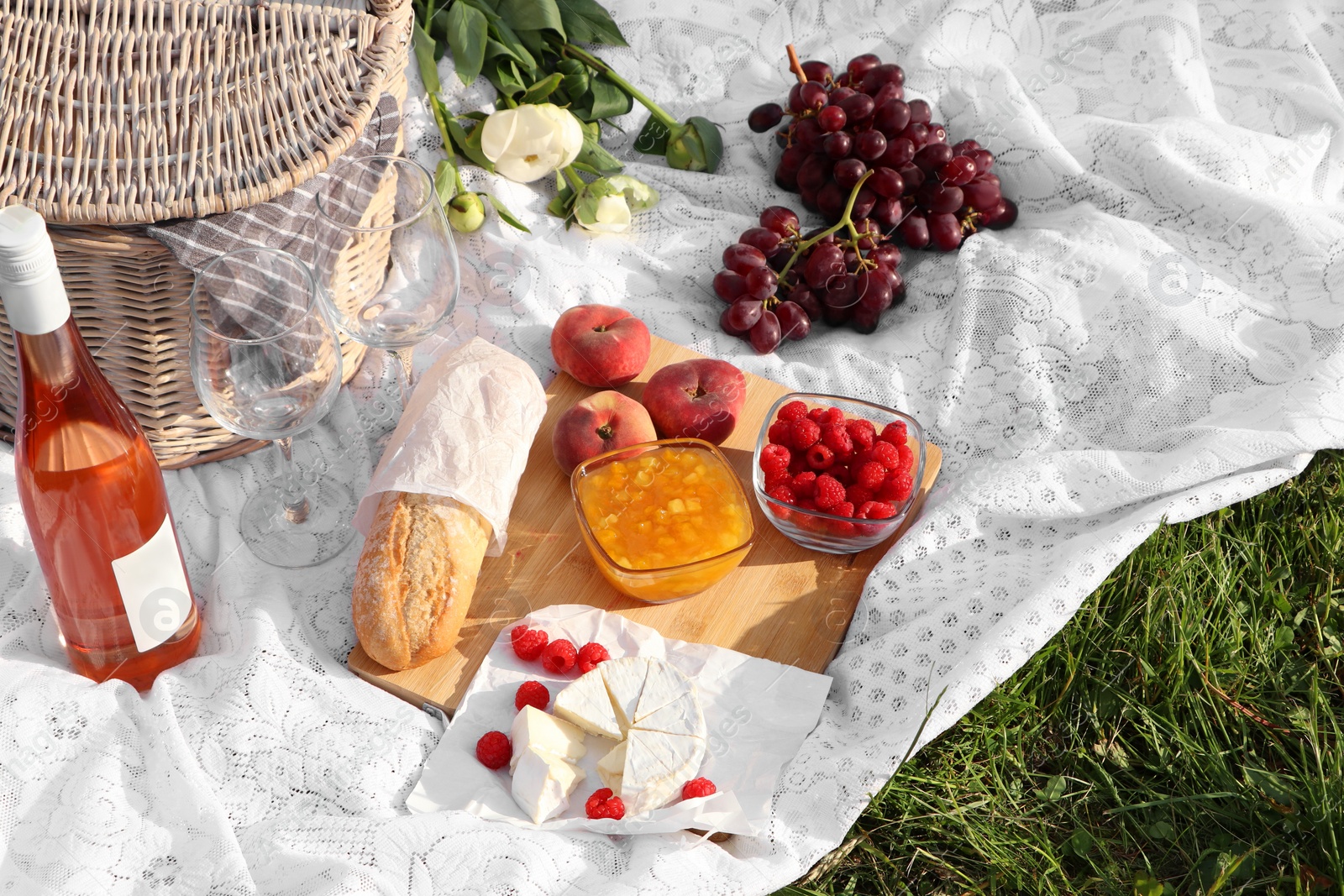 Photo of Picnic blanket with tasty food, flowers, basket and cider on green grass outdoors