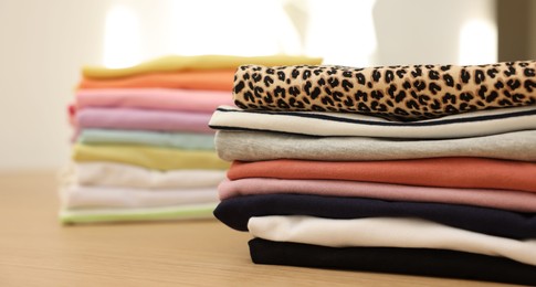 Photo of Many stacked clean clothes on wooden table, closeup