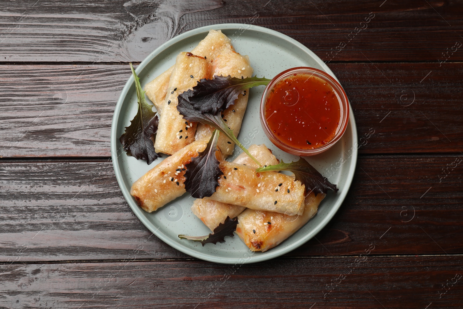 Photo of Tasty fried spring rolls, lettuce and sauce on wooden table, top view