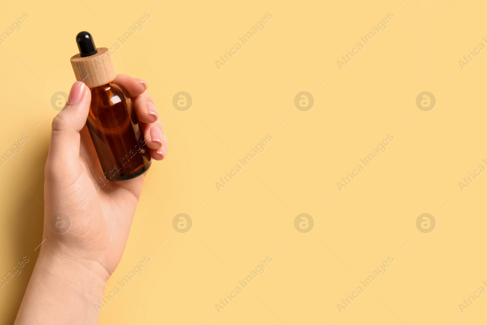 Photo of Woman holding bottle with serum on yellow background, top view. Space for text