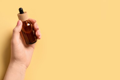 Photo of Woman holding bottle with serum on yellow background, top view. Space for text