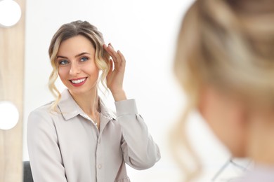 Photo of Smiling woman with beautiful hair style looking at mirror indoors