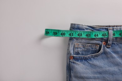 Jeans with measuring tape on light grey background, top view and space for text. Weight loss concept