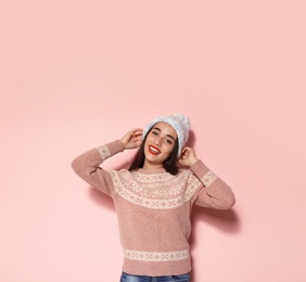 Young woman in warm sweater and knitted hat on color background. Celebrating Christmas