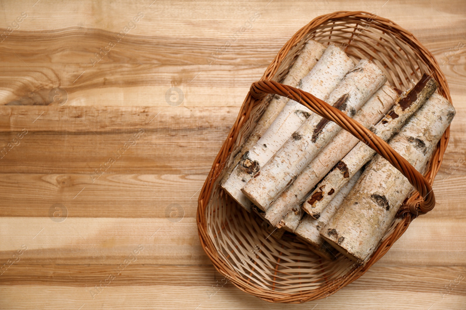 Photo of Wicker basket with firewood on floor indoors, top view. Space for text