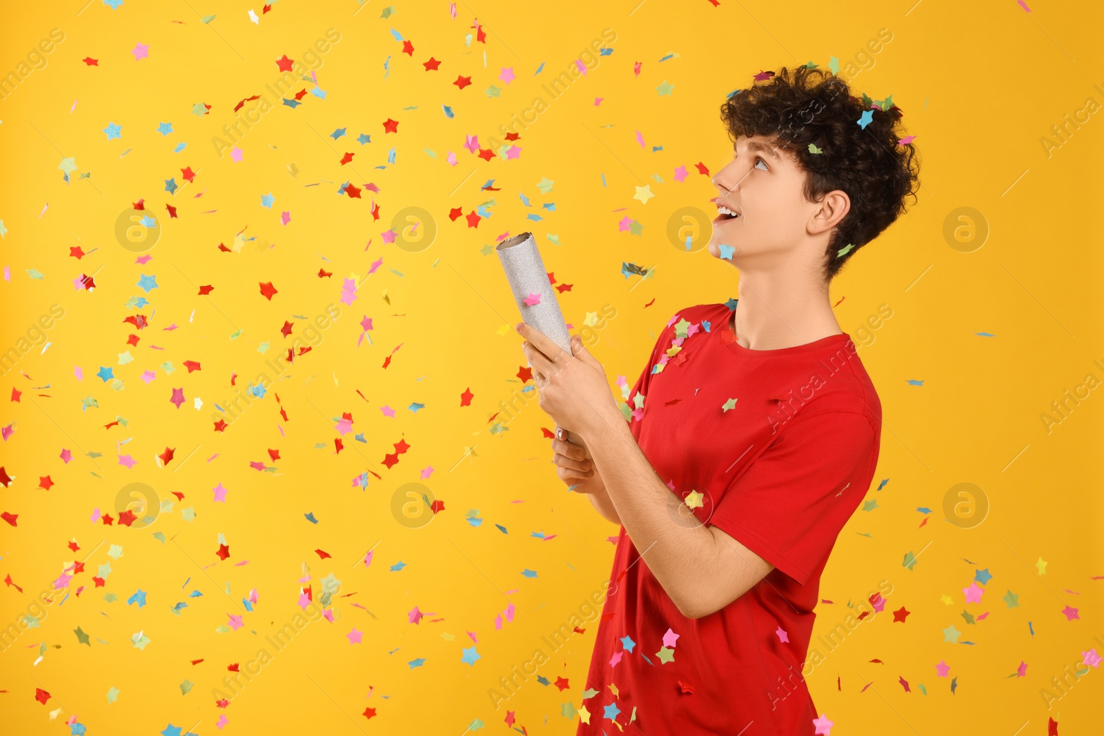 Photo of Happy teenage boy blowing up party popper on orange background