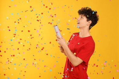 Photo of Happy teenage boy blowing up party popper on orange background