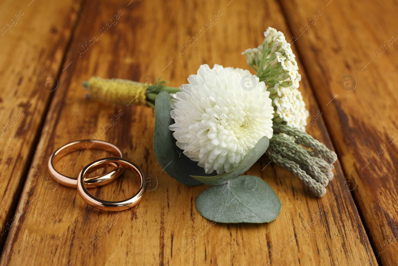 Photo of Small stylish boutonniere and rings on wooden table, closeup