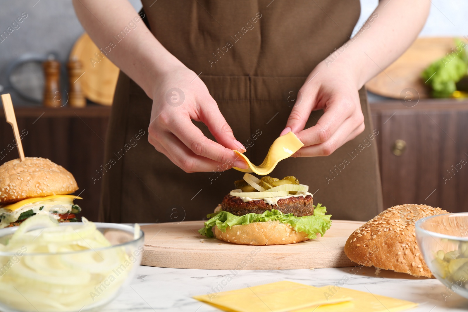 Photo of Woman making delicious vegetarian burger at white marble table, closeup