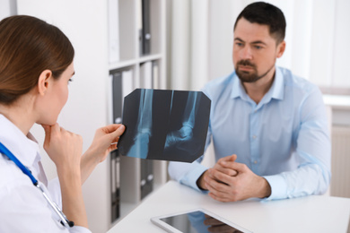 Orthopedist showing X-ray picture to patient at table in clinic