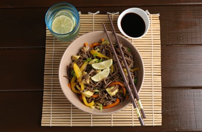 Photo of Stir-fry. Delicious cooked noodles with chicken and vegetables in bowl served on wooden table, flat lay