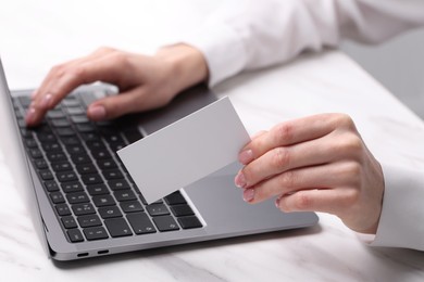 Photo of Woman with laptop holding blank business card at white table, closeup. Space for text