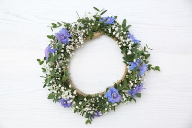 Beautiful flower wreath on white wooden background, top view