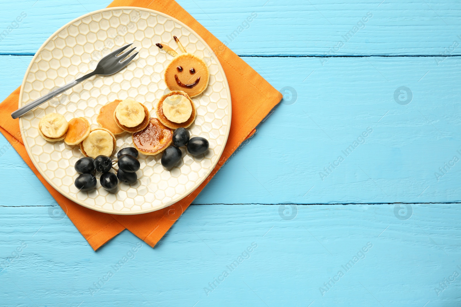 Photo of Creative serving for kids. Plate with cute caterpillar made of pancakes, grapes and banana on light blue wooden table, top view. Space for text