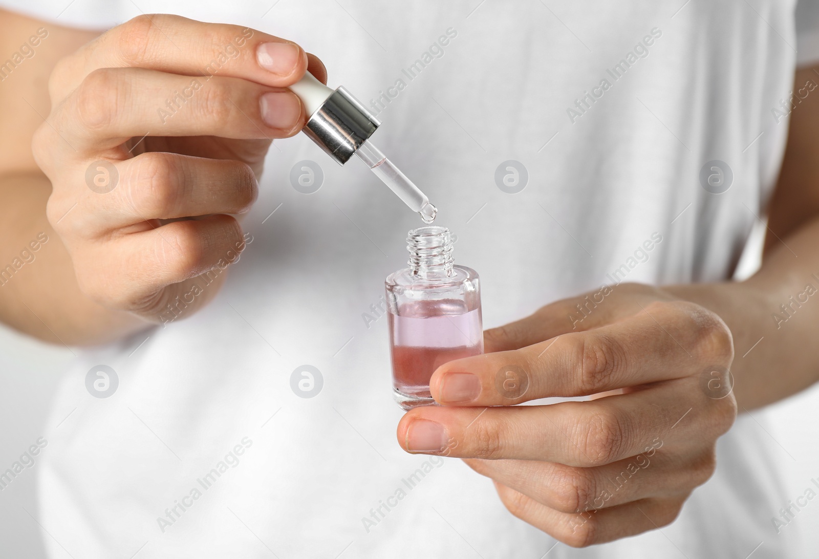 Photo of Young woman dripping rose essential oil into glass bottle, closeup