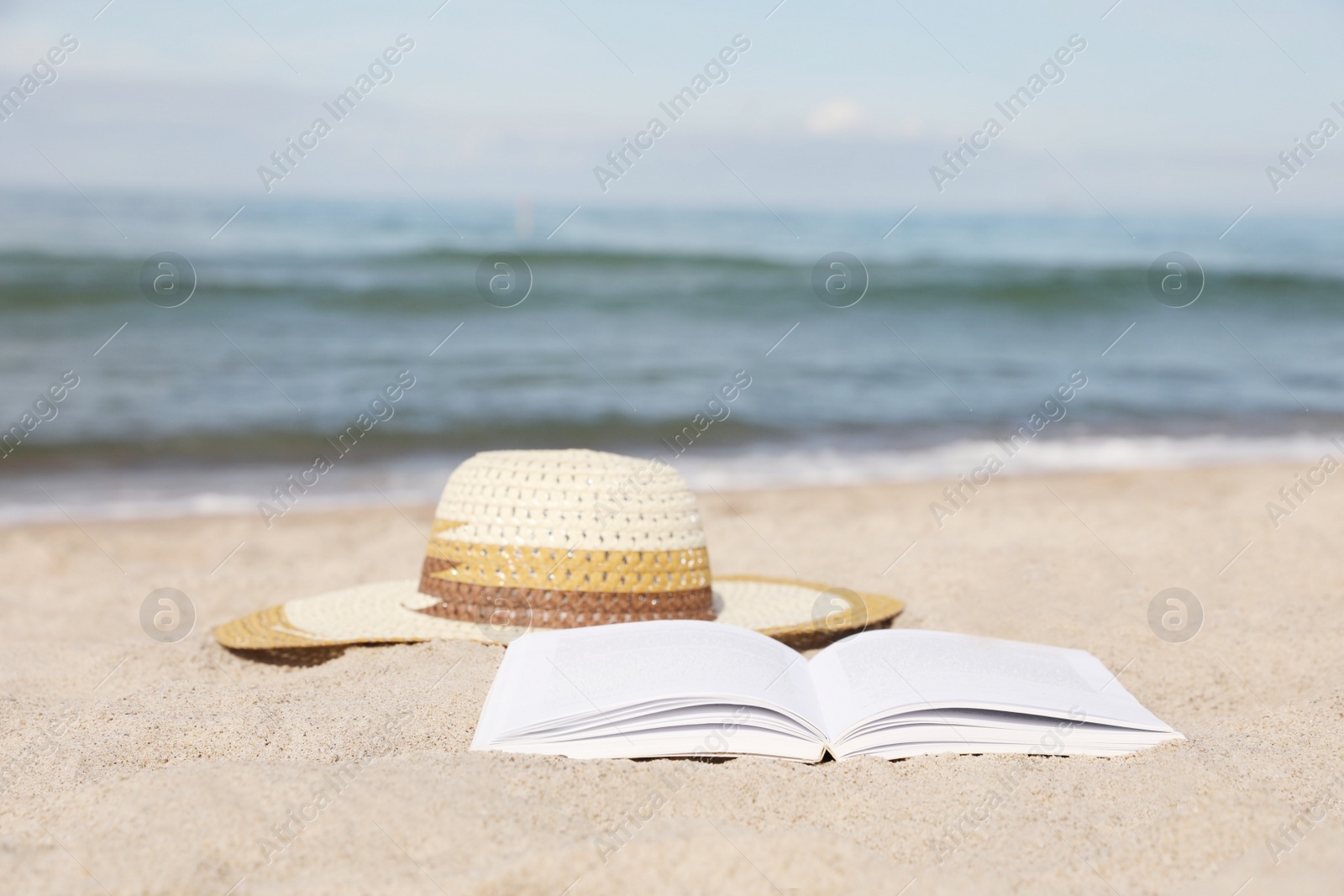 Photo of Open book and hat on sandy beach near sea