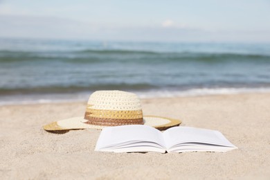 Open book and hat on sandy beach near sea