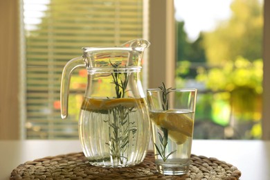 Photo of Jug and glass with refreshing lemon water on light table indoors