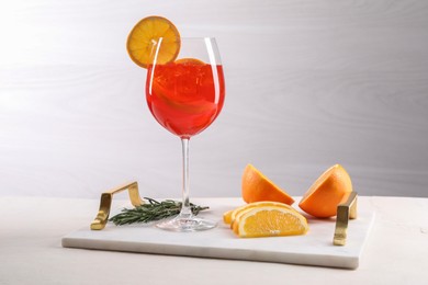 Photo of Glass of tasty Aperol spritz cocktail with orange slices and rosemary on white table against light background