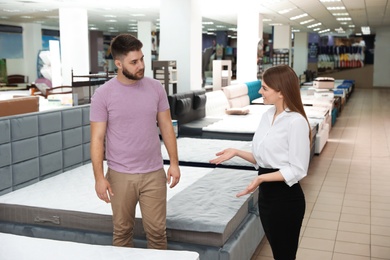 Young saleswoman helping customer to choose new modern orthopedic mattress in store