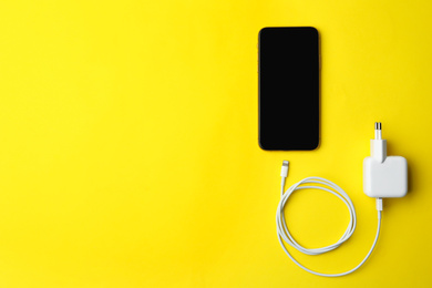 Smartphone and USB charger on yellow background, flat lay. Space for text