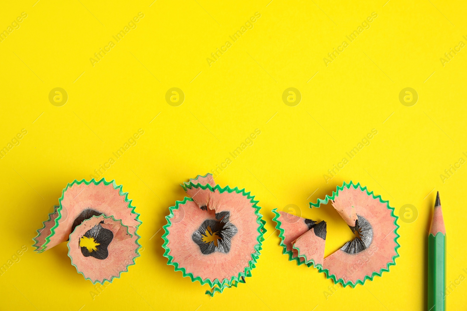 Photo of Pencil and shavings on yellow background, top view. Space for text
