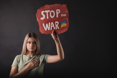 Photo of Emotional woman holding poster with words Stop the War on black background. Space for text