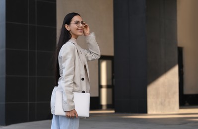 Photo of Happy young woman holding modern laptop outdoors. Space for text