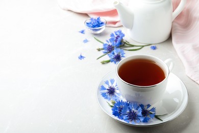 Photo of Cup of tea and cornflowers on light table. Space for text