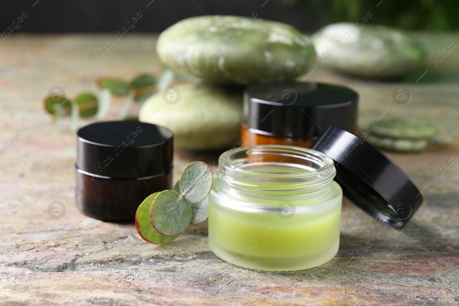 Photo of Jars of cream and eucalyptus leaves on textured table, closeup. Body care products